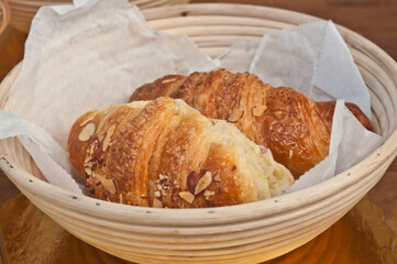 top, front view, close distance two freshly baked almond croissants in a wood wicker basket, on display and for sale at a tropical farmers market