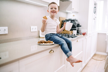 Fototapeta na wymiar little boy drinking tea with cookies in the kitchen