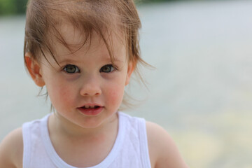 Cute little child kindergarden with gray eyes and short blond hair on a blurred background of a pond
