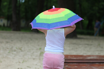 Little child walks along the sandy shore holding a striped rainbow umbrella
