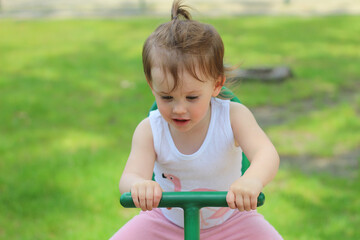 Little laughing preschooler child rides on a swing on the playground against the background of a green lawn