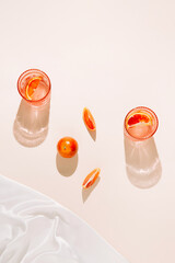 Bloody oranges and glasses of fresh lemonade or water on on pastel beige backgound with white silk cloth. Summer refreshment concept. Sunlit flat lay. Minimal style. Top view