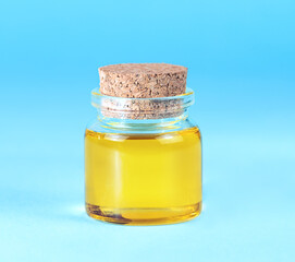 Cosmetic yellow oil in a small glass jar on a blue background.