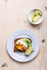 Poached egg on smashed avocado on brown toast served on white plate