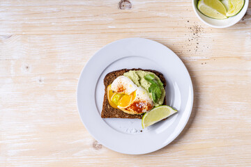 Poached egg on smashed avocado on brown toast served on white plate