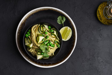 Obraz na płótnie Canvas Bowl of linguine pasta with avocado sauce, green peas, zucchini, sprouts on dark grey table