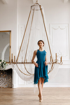 The dancer in a blue dress rests near the chandelier in the white hall
