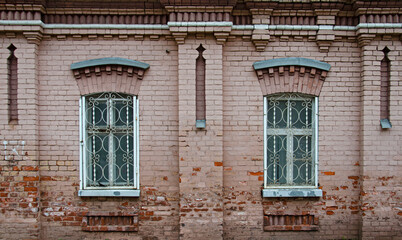 The wall of an old brick pink house. Facade with two windows. Urban architecture. Elements of decoration of the building