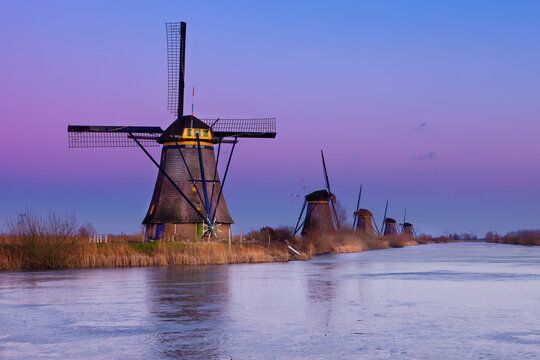 Windmills at Kinderdijk, close to Rotterdam in The Netherlands, in winter with ice on canal at sunset.