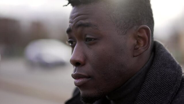 Pensive concerned black African man sitting on city sidewalk curb feeling emotional pain