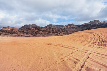 Fototapeta na wymiar Rocky massifs on red desert, vehicle tracks prints in sand, typical scenery in Wadi Rum, Jordan