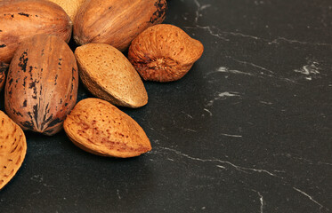 Closeup of almonds and pecan nuts in shell on dark board. Space for text on right side