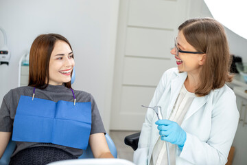 Fototapeta premium A woman patient sits in a dental chair at a dentist doctor's appointment. A girl with a beautiful smile and white even teeth.