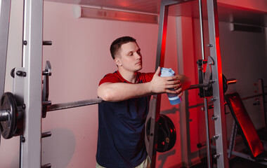 the athlete after training stands near the barbell and holds a shaker with a protein shake.
