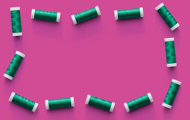 Border of flat-lying spools of green thread on pink background