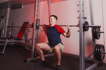 male athlete squats with a barbell in the gym with a tense face