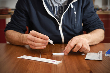 man in a jaket makes a rapid test for antibodies to coronavirus covid 19 at home. He opened a rapid test kit, and dropes a drop of analysis solution onto the rapid antigen test