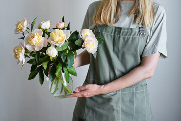 Peonies in a vase in the hands of a happy woman. Stylish white peonies in florist hand. The florist girl gathered a bouquet. Beautiful spring white flowers. Gift for the holiday. Fresh floral