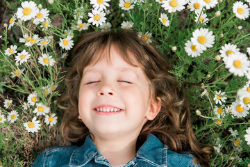 Little cute girl lies on the field with daisies. Sunny day. Having fun and enjoy life. Top view