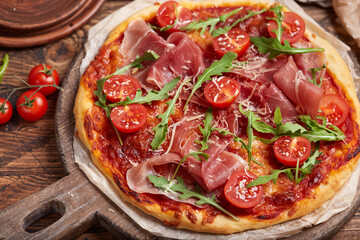 Pizza with prosciutto meat, cherry tomatoes, arugula, mozzarella and parmesan cheese. Freshly baked homemade pizza.