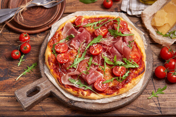 Pizza with prosciutto meat, cherry tomatoes, arugula, mozzarella and parmesan cheese. Freshly baked homemade pizza.