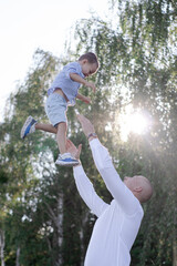 Bald dad tosses up son in the field or forest on a sunny summer day. father's day.