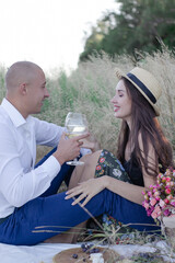 husband and wife on a romantic date on a picnic drinking wine. happy couple. brunette and bald man in the field.