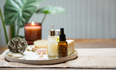 Fototapeta na wymiar clean organic skincare and bodycare products with oil bottle, serum, natural soap and quartz roller with candle and green plants in the background