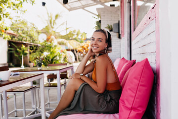 Attractive lady laughing outside. Happy woman in bright t-shirt and skirt and scarf smiling on background of street cafe