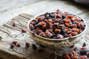 Dried grapes in silver bowl on wooden background, raisins