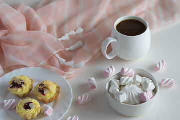 White porcelain cup of black strong hot coffee, tea on a light background with delicate marshmallows and cakes, homemade cakes. Beautiful table setting, serving dishes 
