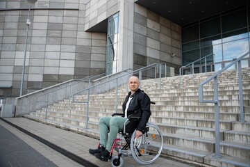 Young handsome man in a wheelchair waiting for help at the bottom of a stairs.