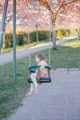 A little cute girl is riding a swing in a blooming garden. Spring.