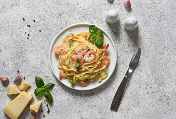 Tagliatelle pasta with creamy sauce, parmesan and shrimps in a plate on a concrete background. View from above.