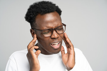 Sick African American millennial man suffering from tinnitus, throbbing earache, tired of noise....