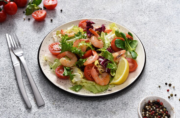 Mix salad with tomatoes and grilled shrimps with sauce and clematis on the kitchen table. Concrete food background.