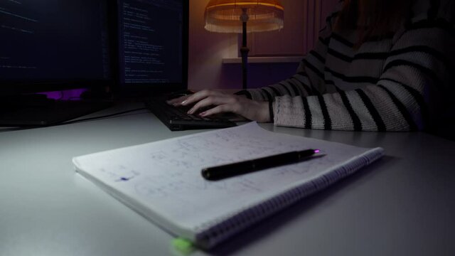 Young caucasian woman is sitting in front of computer and coding new program typing on keyboard. Female worker of IT support is doing her job. She is writing new html lines. Developing software theme.