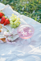 Spring picnic in nature. A glass of pink champagne with sakura flowers, a wicker bag, a hat, Italian. Wine. Spring.