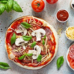 Cooking Italian pizza with tomato sauce, fresh tomatoes, cheese, mushrooms, salami slices  and basil . Fresh food cooking concept at home. Semi-finished product, raw dough.