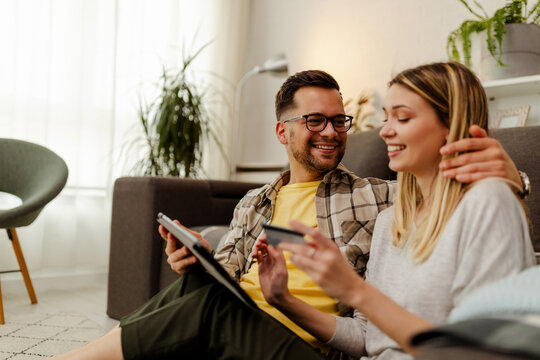 Image of a happy young loving couple at home on floor near sofa using tablet computer.