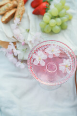 Spring picnic in nature. A glass of pink champagne with sakura flowers, a wicker bag, a hat, Italian. Wine. Spring.