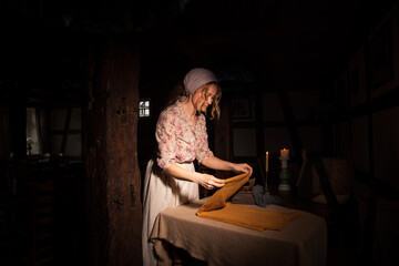 Obraz na płótnie Canvas Eine Frau Mitte Vierzig, ende Achtzehn Jahrhundert bügelt mit dem alten verrosteten Bügelleiser die Bekleidung. Sie ist überarbeitet. Die Frau hat Kopftuch und Schurze an. Die Gebäude ist altmodisch 