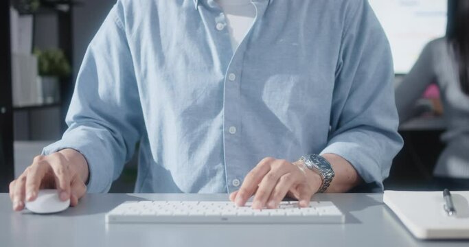 Asian man using desktop computer in home office with business partner, close up hand typing keyboard and mouse click. People working at home or internet information technology concept. Panning