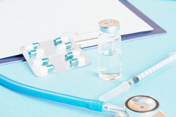 vaccination concept, syringe, medicine vial and stethoscope on light blue background cop space doctor desk