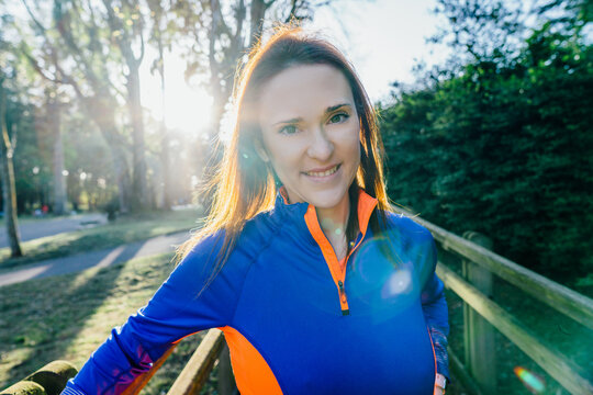 Portrait of young beautiful athlete woman backlit with flare looking at camera at sunset in spring or summer in a wooded park. corporate image concept. woman and sport