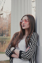 Stylish, confident girl looks into the distance. Pink glasses. Striped black and white jacket....
