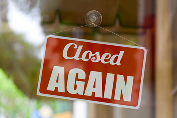 Close-up on a red sign in the window of a shop displaying the message: Closed again.
