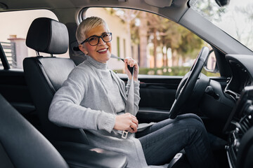 Fototapeta na wymiar Portrait of happy senior woman fastening seat belt before driving a car.