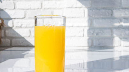 Yellow lemonade in a glass against a white brick wall background. Orange juice in a glass