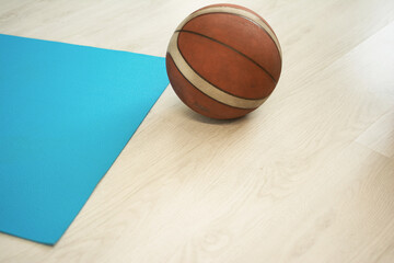 A yoga mat nearby. A basketball ball made of rubber is on the rustic floor close-up. The concept of sports equipment for everyday activities for a healthy start to the day and its active continuation.